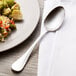 A Chef & Sommelier stainless steel dinner spoon next to a plate of food.