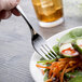 A hand holding a Chef & Sommelier stainless steel salad fork over a plate of salad.