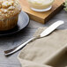 A muffin on a plate with a knife and napkin.