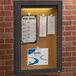 An Aarco bronze indoor lighted bulletin board cabinet with a hinged locking door.