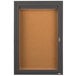 An Aarco brown cabinet with a key and a cork board inside.