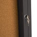 A bronze anodized Aarco bulletin board cabinet with a key in the lock.