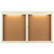 A white framed Aarco bulletin board cabinet with two enclosed glass doors and lights.