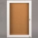 A white cabinet with a cork board and glass door with a key.