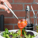 A hand using an Arcoroc stainless steel sauce ladle to pour sauce over a bowl of salad.