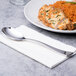 A Chef & Sommelier stainless steel dinner spoon on a napkin next to a plate of food.