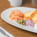 A Schonwald white porcelain oval platter with bread, salmon, and cheese on a table.