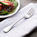 A Chef & Sommelier stainless steel salad fork on a napkin next to a plate of salad.