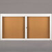 A white Aarco bulletin board cabinet with two doors and a cork board inside.
