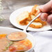 A person holding a Chef & Sommelier stainless steel soup spoon over a bowl of soup.