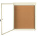A white frame enclosed bulletin board with a cork board inside and a white door.