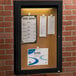 An Aarco black enclosed bulletin board cabinet with paper on it.