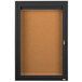 A black cabinet with a cork bulletin board inside and a key lock.