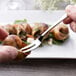 A hand holding an Arcoroc stainless steel escargot fork over a snail shell.