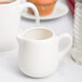 An American Metalcraft white porcelain creamer with a handle on a white surface.