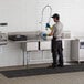 A man washing dishes in a Regency 3 compartment sink in a kitchen.