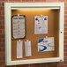 An ivory indoor enclosed bulletin board with a cork surface with papers attached.
