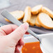 A person's hand holding a Libbey stainless steel bouillon spoon over soup.