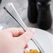 A hand holding a Libbey Minuet stainless steel dinner fork over a plate of food.