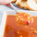 A hand holding a World Tableware stainless steel bouillon spoon filled with soup over a bowl of soup.