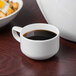 A Schonwald white porcelain espresso cup filled with coffee on a table next to a bowl of food.