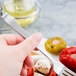 A hand holding a Libbey stainless steel cocktail fork over a plate of food.