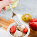 A Libbey stainless steel cocktail fork in a bowl of mozzarella cheese, tomatoes, and peppers.