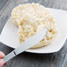 A person using a Libbey stainless steel butter spreader to spread butter on a biscuit on a plate.