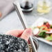 A hand holding a Libbey stainless steel iced tea spoon in a glass with a salad.