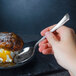 A hand holding a Libbey stainless steel dessert spoon over a dessert.