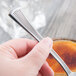 A person's hand holding a Libbey Minuet stainless steel teaspoon over a bowl of liquid.