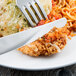 A Libbey stainless steel dinner knife and fork cutting food on a plate.