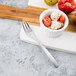 A Libbey stainless steel cocktail fork in a bowl of tomatoes and cheese on a cutting board.