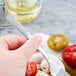 A person's hand holding a Libbey stainless steel cocktail fork over a bowl of food.