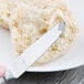 A Libbey stainless steel bread and butter knife spreading butter on a biscuit.