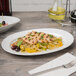 A Schonwald white porcelain oval platter with food on it and silverware.