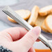 A hand holding a Libbey stainless steel bouillon spoon over a bowl of soup.