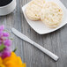 A knife next to a plate of biscuits and a cup of coffee on a table.