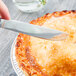 A hand holding a Libbey stainless steel dessert knife cutting a pie.