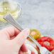 A hand holding a Libbey Minuet cocktail fork over a white bowl of food.