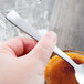 A hand holding a Libbey stainless steel teaspoon over a glass of liquid.