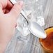 A hand holding a Libbey stainless steel teaspoon over a cup of coffee.