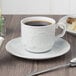 A white saucer with a cup of coffee on it.
