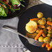 A Libbey stainless steel dinner fork next to a plate of food with carrots and potatoes.