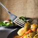 A Libbey stainless steel dinner fork sticking out of food on a plate.