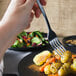 A hand holding a Libbey Oceanside dinner fork over a plate of food.