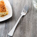 A Libbey stainless steel utility fork next to a piece of cake on a plate.