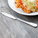 A Libbey stainless steel dinner knife with a fluted blade on a table with a plate of spaghetti, meat, and cheese.