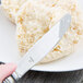 A Libbey stainless steel bread and butter knife with a plain blade cutting a piece of bread.
