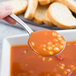 A person holding a Libbey stainless steel bouillon spoon full of soup.